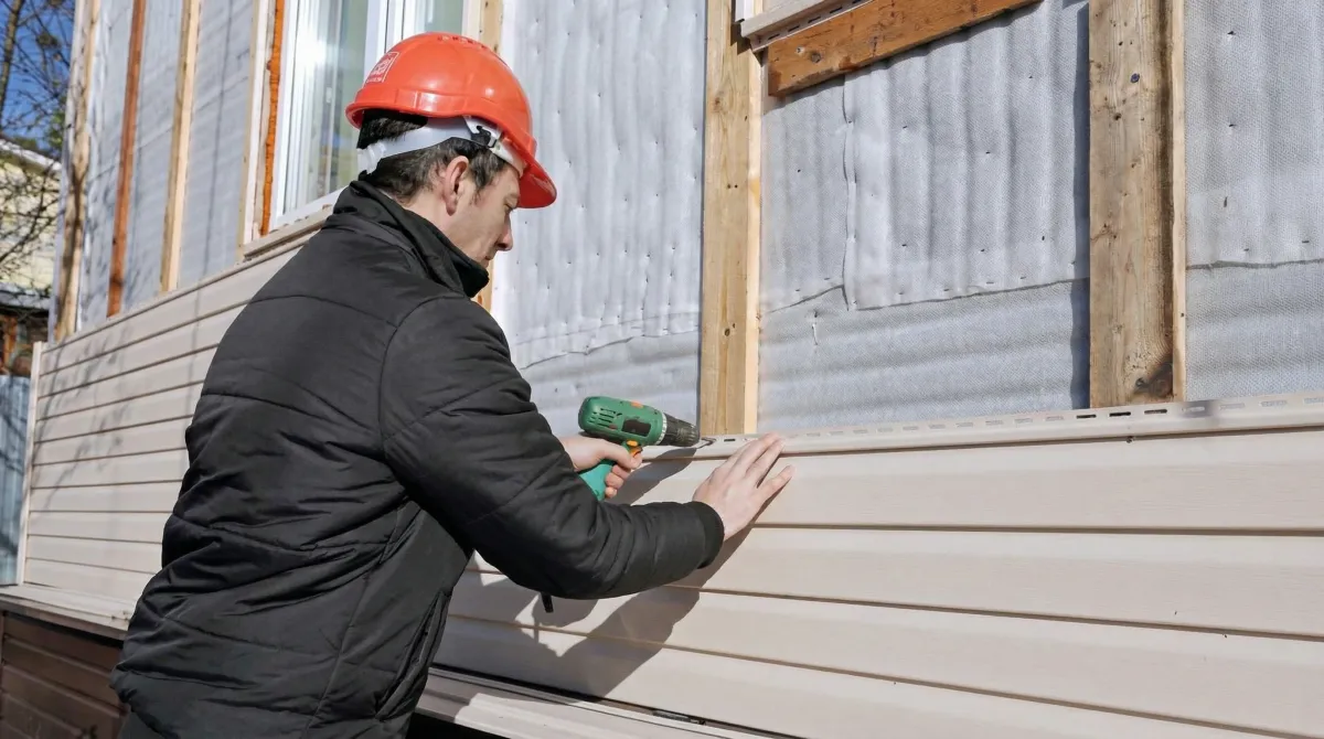 Siding replacement professional using a power drill to install new tan vinyl siding on a home exterior in Wilmington, NC